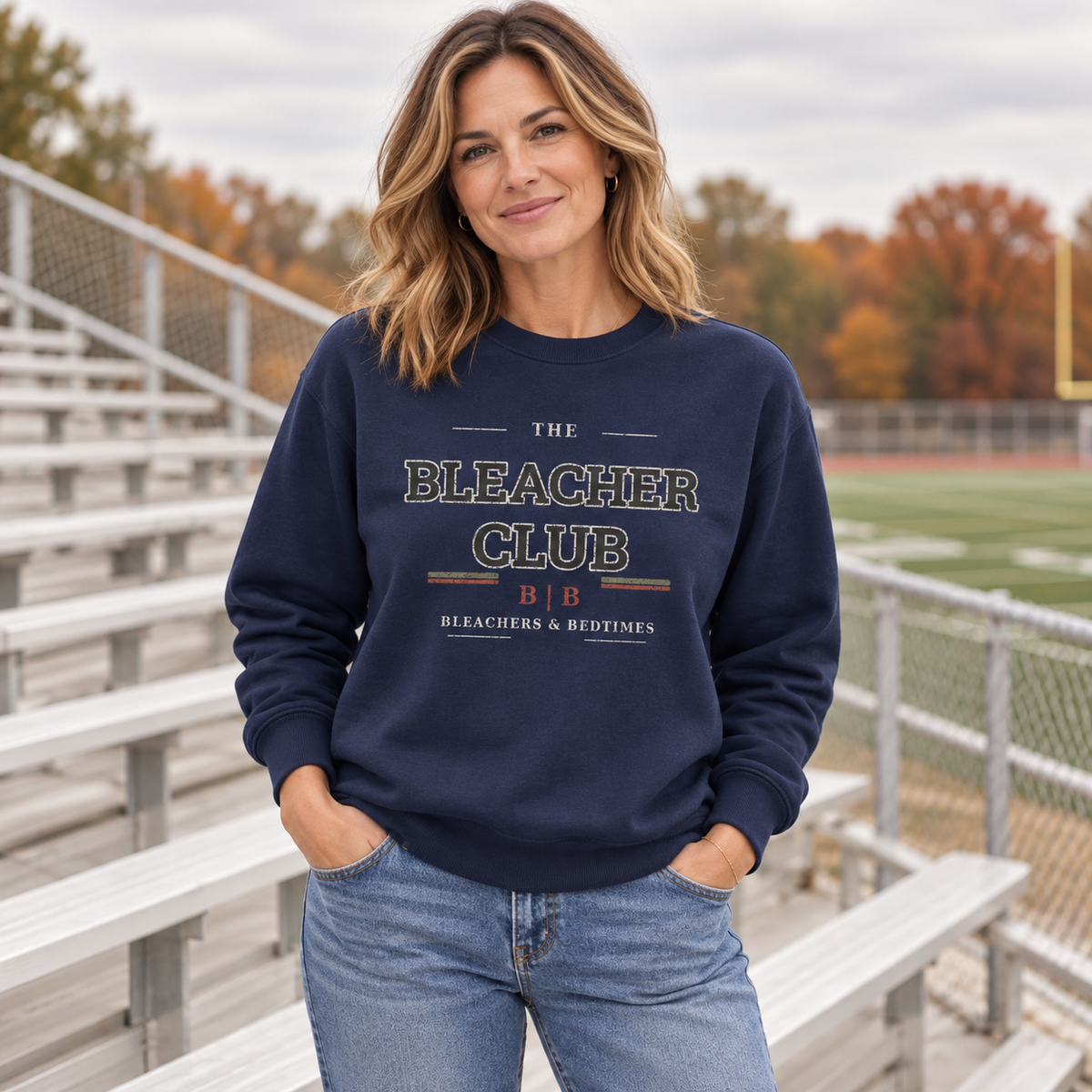 Woman wearing The Bleacher Club true navy crewneck beside outdoor sports bleachers