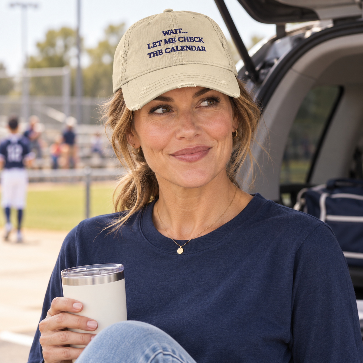 Woman wearing the khaki Wait Let Me Check the Calendar hat while holding coffee