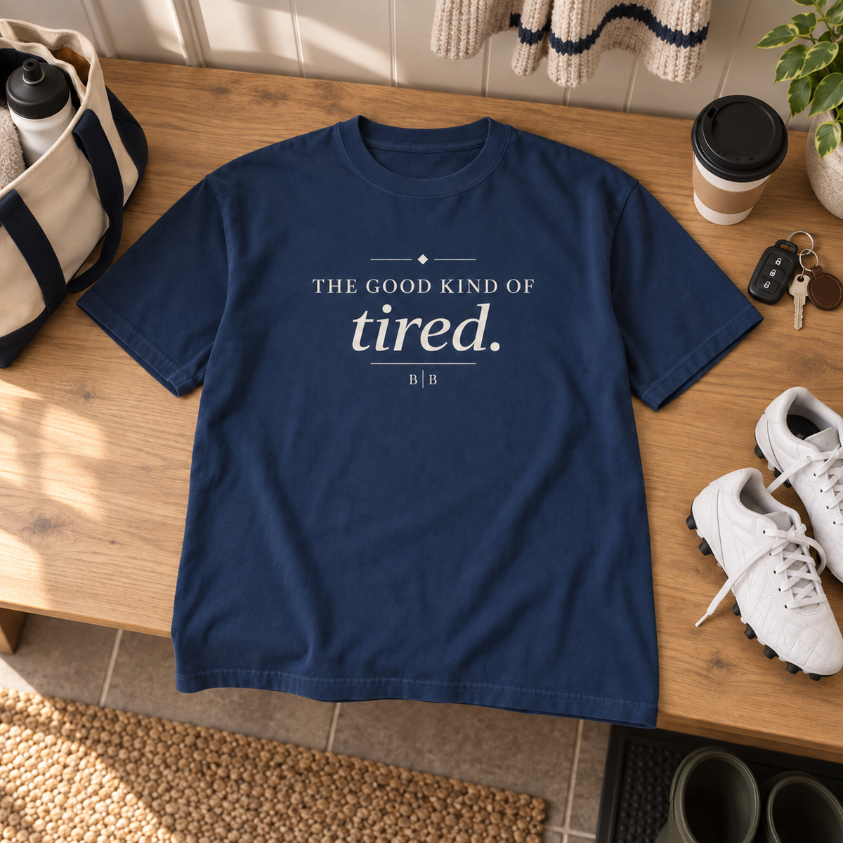 The Good Kind of Tired navy T-shirt styled with sports gear, coffee, and car keys